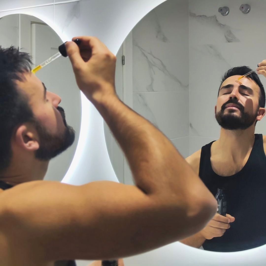 Hombre aplicando el serum Dark Spots Fighter de Homo Naturals durante su rutina facial para obtener resultados visibles antiarrugas, gracias a una hidratación profunda que se consigue con su complejo de dos ácidos hialurónicos (peso bajo molecular y muy bajo peso molecular), así como la reducción de manchas, gracias a la vitamina C y el complejo despigmentante w3+, y favorecer una piel con un tono más uniforme.